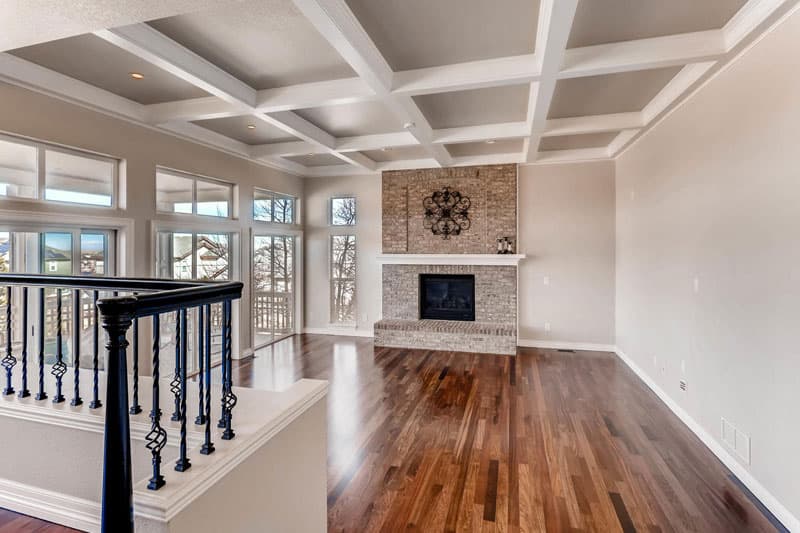 Living room painted by BrothersPaint.com: white coffered ceiling, stacked-stone fireplace, and hardwood floors